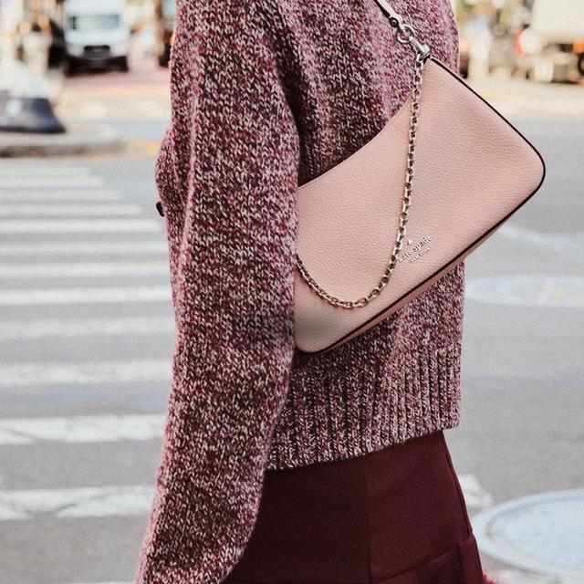 Woman carrying a pink leather crossbody bag with chain strap while wearing a burgundy sweater and skirt.