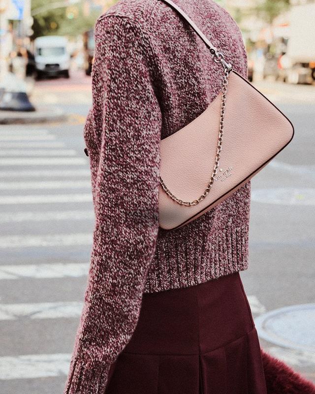 Woman carrying a pink leather crossbody bag with chain strap while wearing a burgundy sweater and skirt.