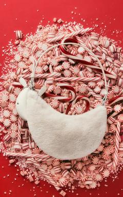 White fuzzy handbag surrounded by red and white striped peppermint candies and candy canes.