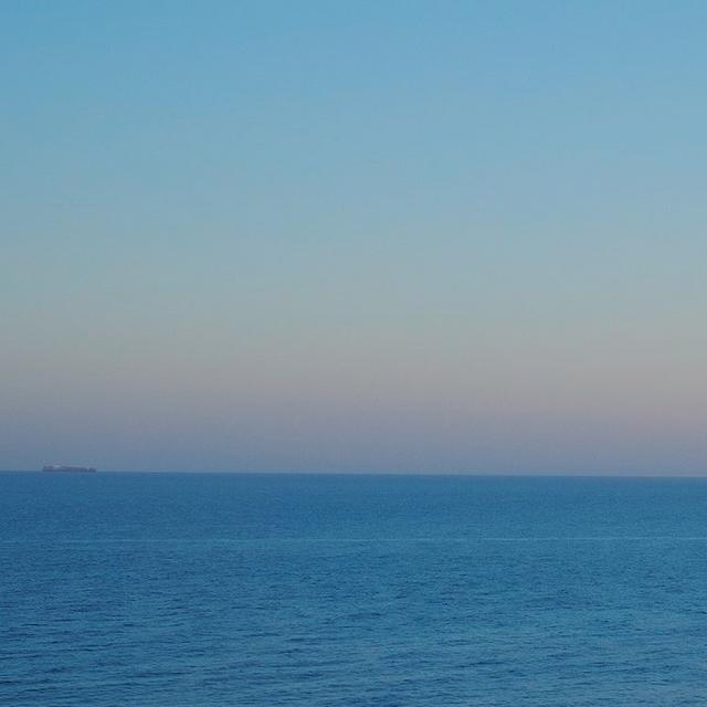 Calm ocean view at dusk with a ship visible on the distant horizon.