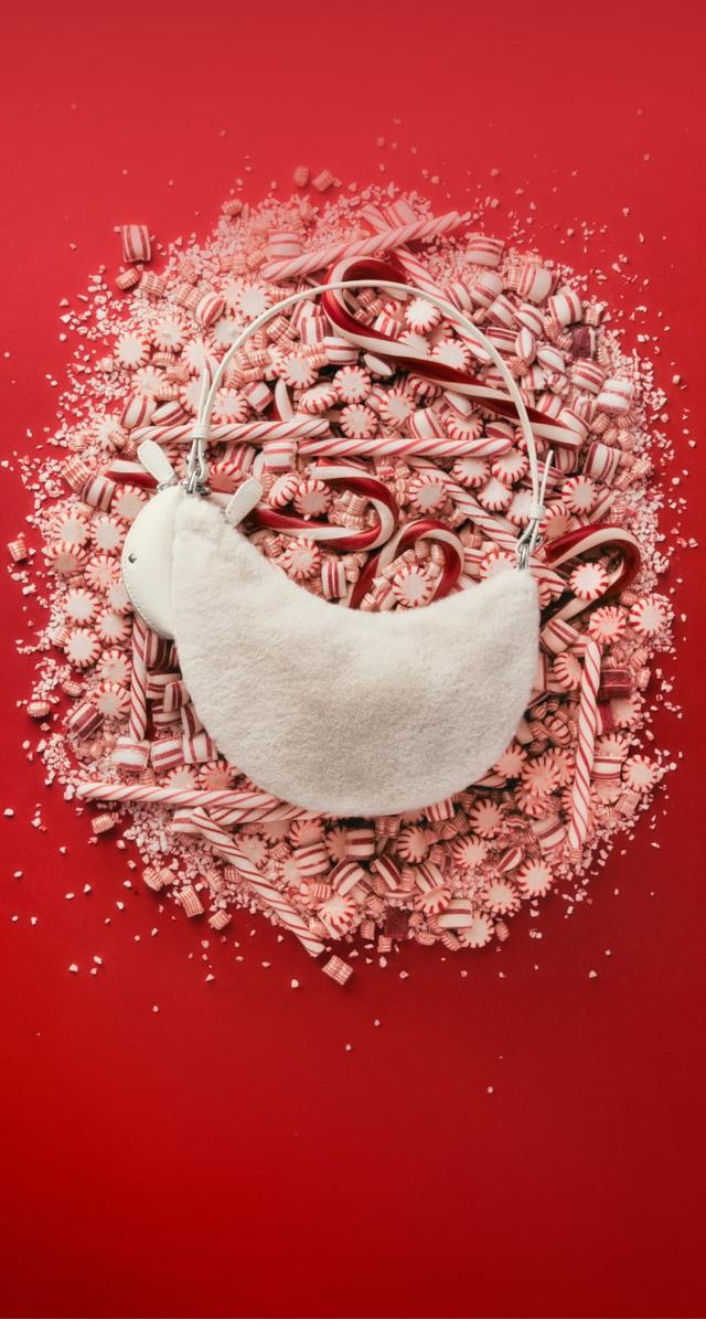 White bowl overflowing with peppermint candies and candy canes on red surface with scattered sprinkles.