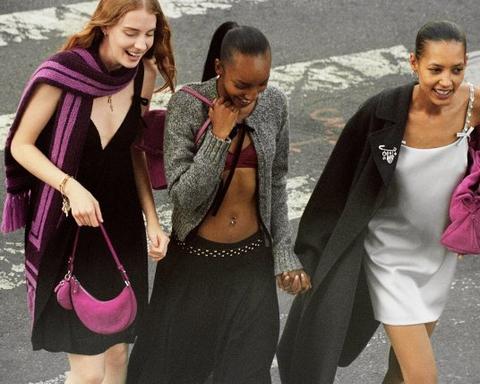 Three women walking together outdoors, laughing and holding hands, wearing casual dresses and coats.