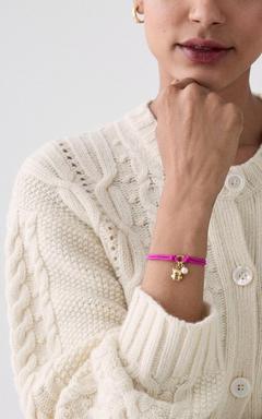 Person wearing cream cable-knit cardigan with a bright pink bracelet featuring a gold charm.