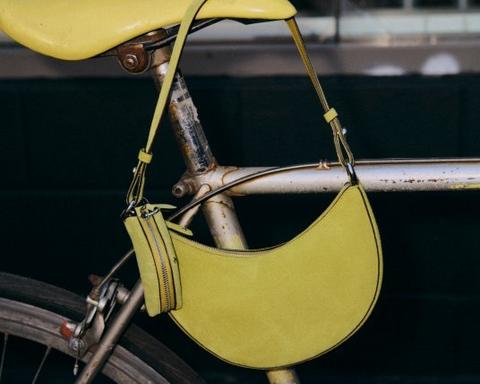 Yellow crescent-shaped shoulder bag with tassel detail hanging on vintage bicycle frame.