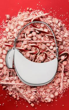 White crescent-shaped shoulder bag with tassel detail resting on red and white striped peppermint candies.