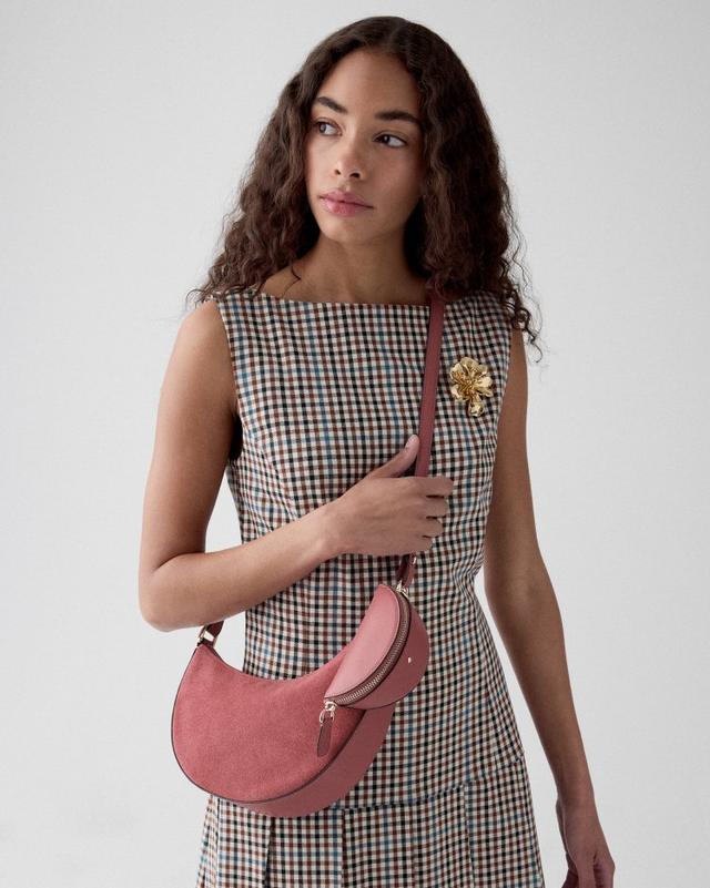 Woman wearing sleeveless gingham check dress with gold brooch, holding a pink crescent-shaped crossbody bag.