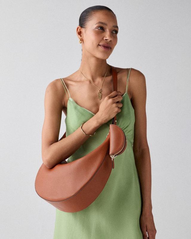 Woman wearing green slip dress holding brown leather crescent-shaped shoulder bag.