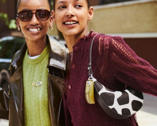 Two smiling women wearing textured knitwear, one in a lime green sweater and one in a burgundy cardigan.