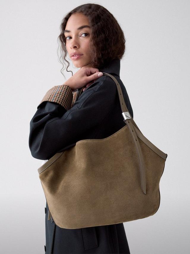 Woman wearing a black jacket with plaid collar, carrying an olive green suede shoulder bag.