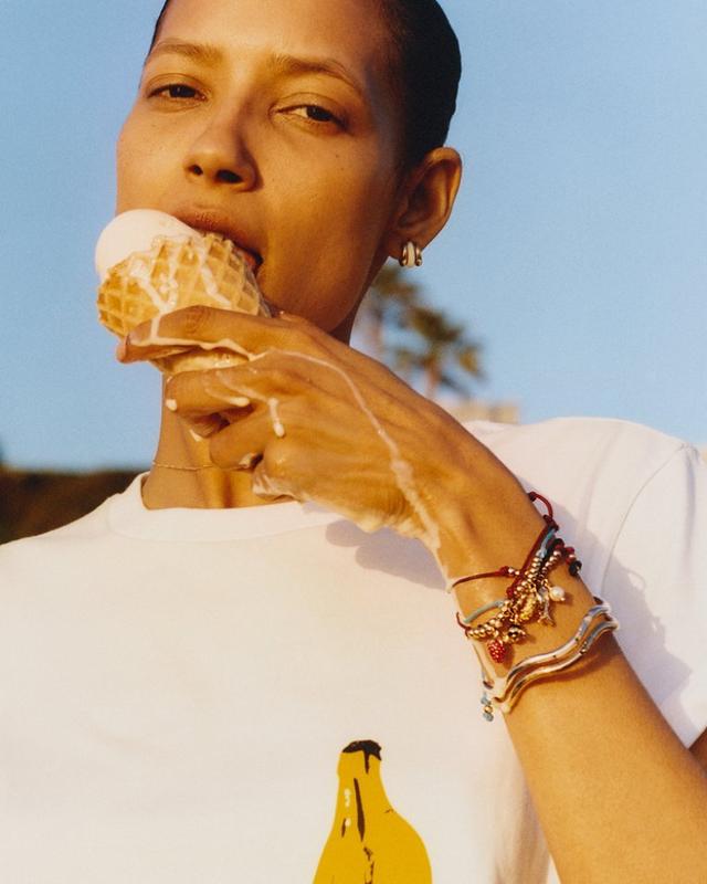 Woman wearing colorful beaded bracelets eating an ice cream cone outdoors on a sunny day.