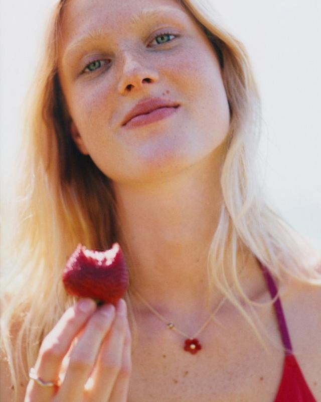 Woman with freckles holding a bitten red apple while wearing a delicate gold necklace.