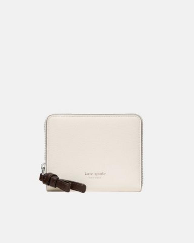 kate spade new york cream leather zip-around wallet with dark brown tassel detail.