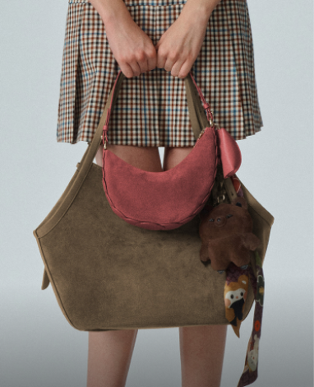 Person holding a large olive green canvas tote bag with a pink suede crescent bag layered on top.