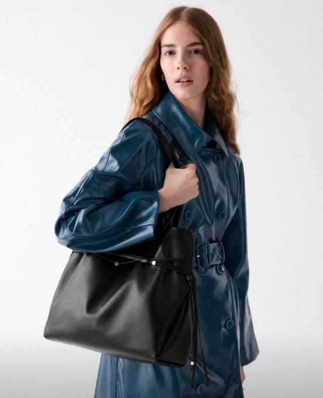 Woman wearing a blue leather trench coat with belt, carrying a black leather shoulder bag.