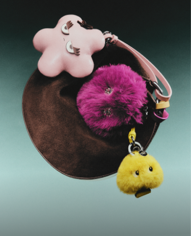 Brown circular pouch with pink flower-shaped top and keychain charms including magenta pom-pom and yellow chick.