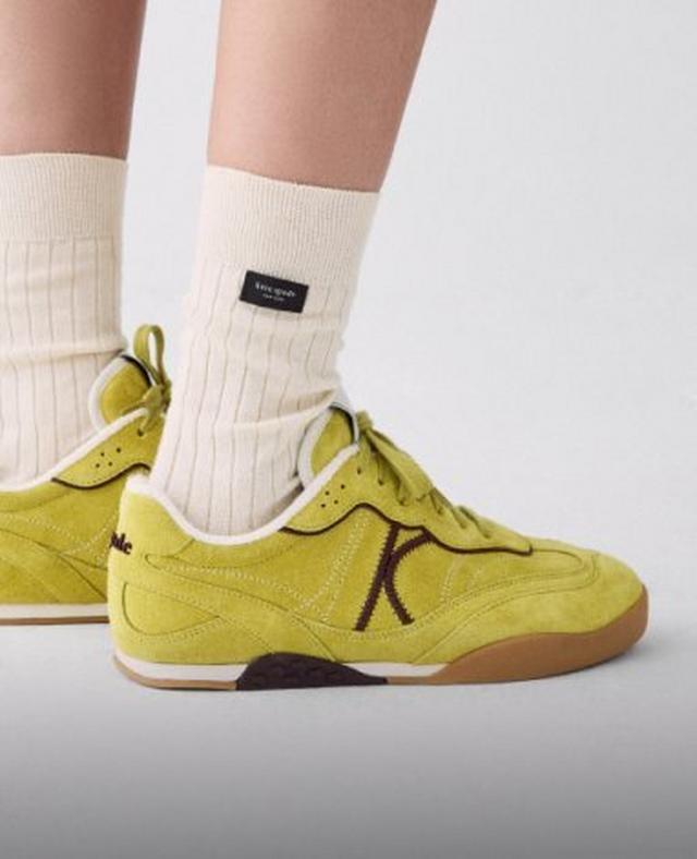 Person wearing cream ribbed socks with a small black label and yellow sneakers with brown K logo.