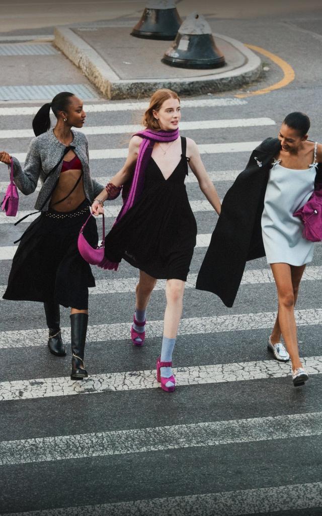 Three women walking together outdoors, smiling and wearing coordinated outfits with pink accessories.