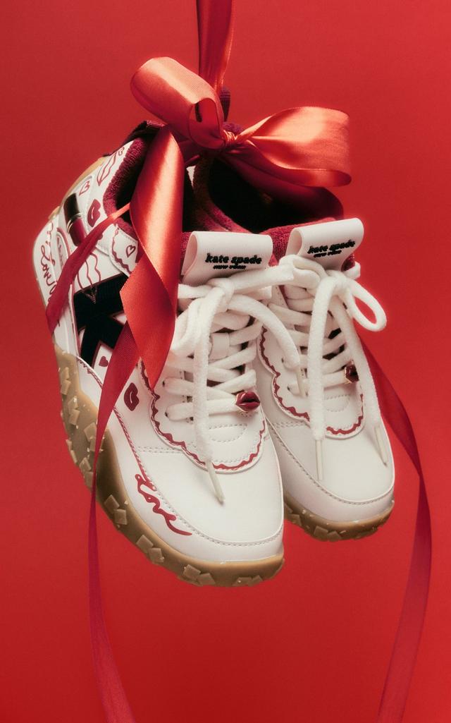 Kate Spade white sneakers with red scalloped trim and red satin ribbon laces tied in a bow.