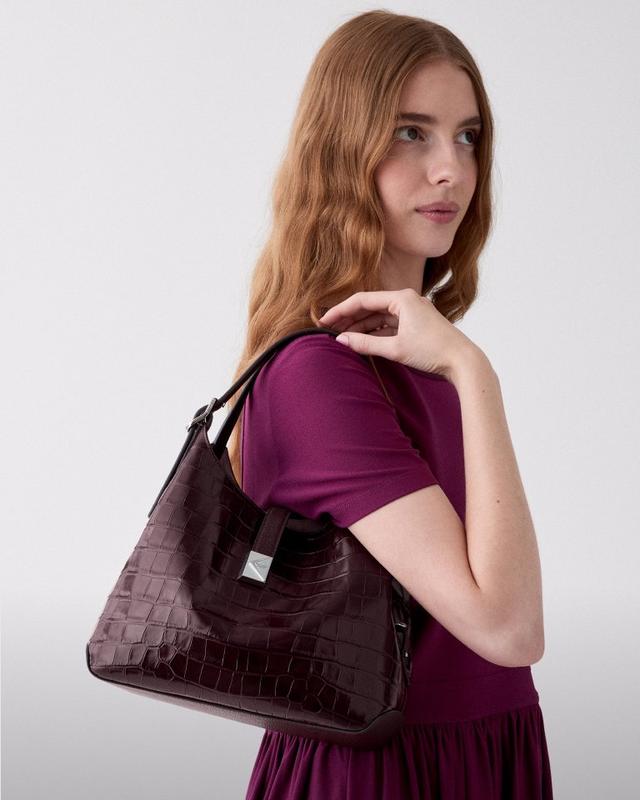 Woman wearing purple dress carrying a brown croc-embossed shoulder bag over her shoulder.