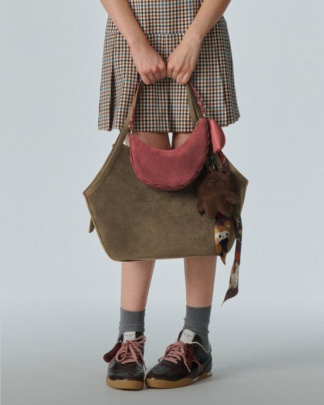 Person wearing plaid dress holding olive green and pink tote bag with stuffed animal attached.