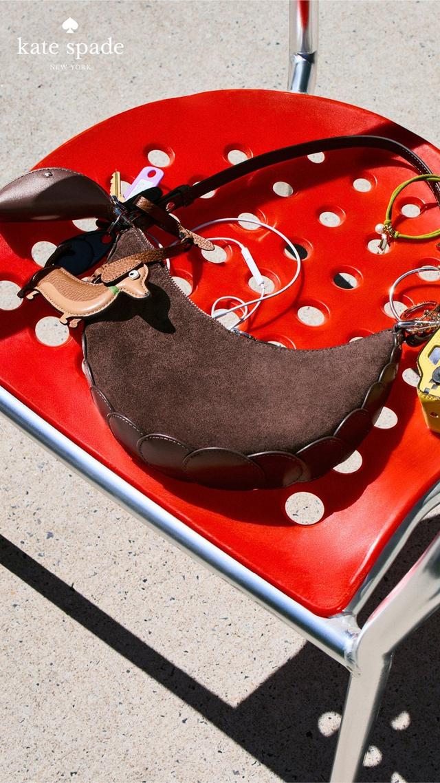 Kate Spade brown suede crescent shoulder bag with scalloped edges on red polka dot tray with accessories.