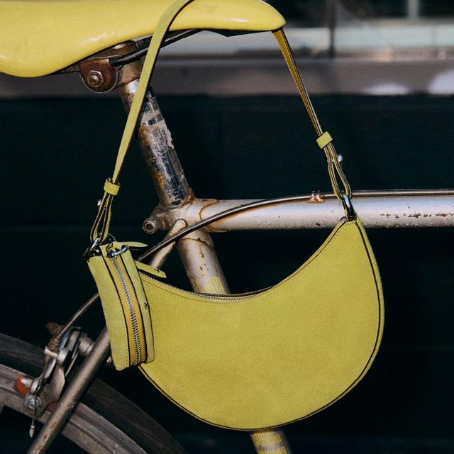 Yellow crescent-shaped shoulder bag with zippered pouch hanging on vintage bicycle frame.