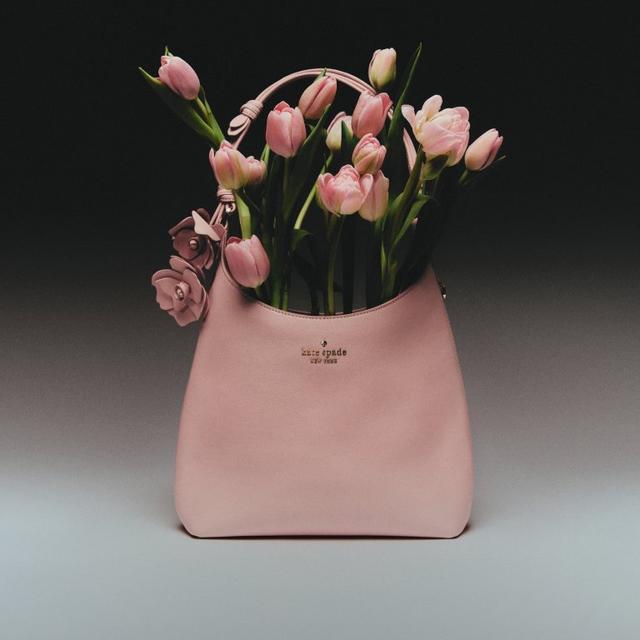 Kate Spade pink leather hobo bag with floral charm detail, displayed with fresh pink tulips.