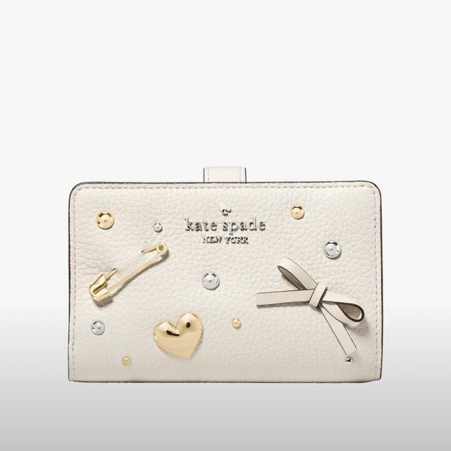 Kate Spade cream leather wallet with decorative safety pin, heart charm, and studded embellishments.