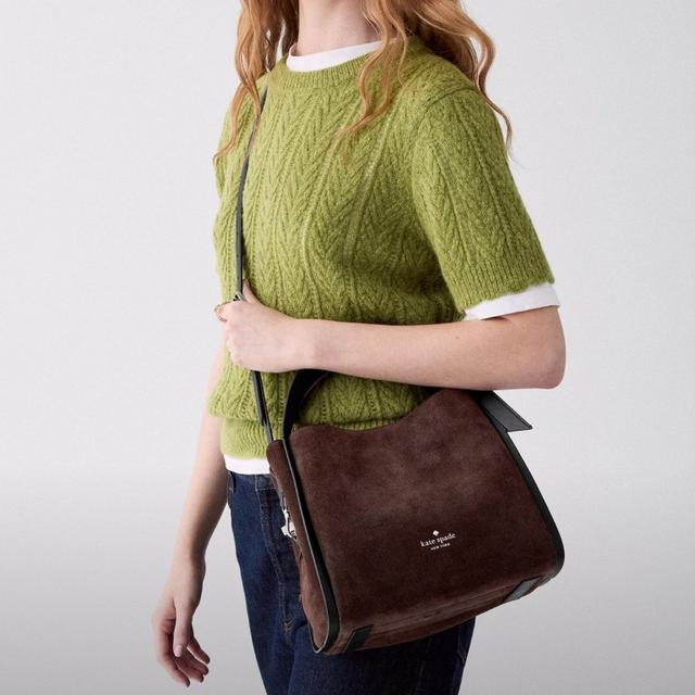 Woman wearing green cable-knit sweater vest over white tee with brown Kate Spade crossbody bag.