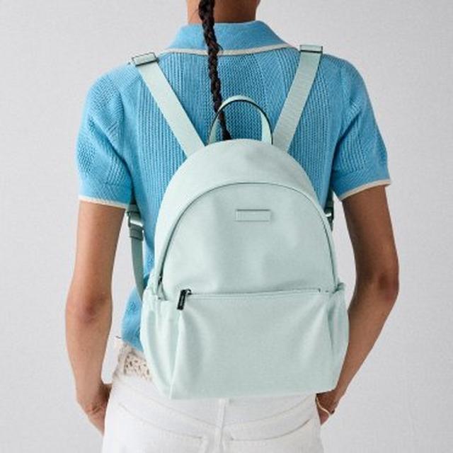 Person wearing a light blue backpack over a blue knit polo shirt and white pants.