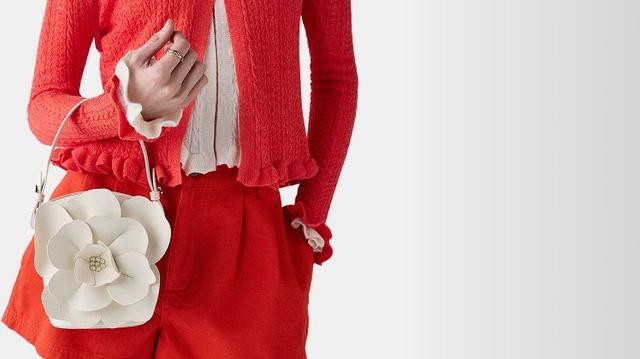 Woman wearing red jacket and shorts, holding the Kate Spade Outlet white flower-shaped crossbody bag