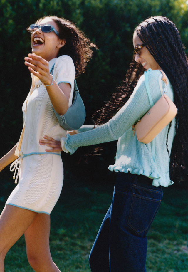 Two women laughing together outdoors and three Kate Spade crossbody bags stacked in tan, floral, and blue.