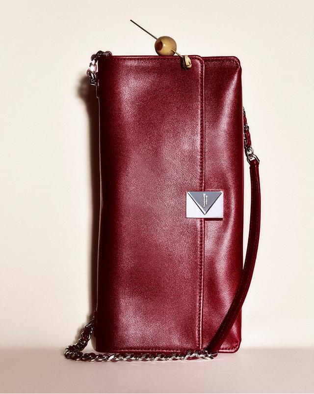 Elegant red leather clutch with a silver chain strap, featuring a sleek design and a geometric clasp. The background is a soft cream color, conveying sophistication.