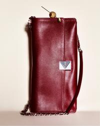 Elegant red leather clutch with a silver chain strap, featuring a sleek design and a geometric clasp. The background is a soft cream color, conveying sophistication.