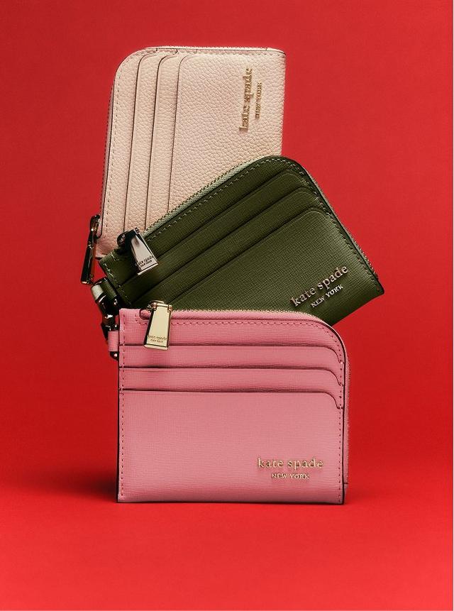 Three kate spade new york card holders stacked together in pink, olive green, and beige with gold branding.