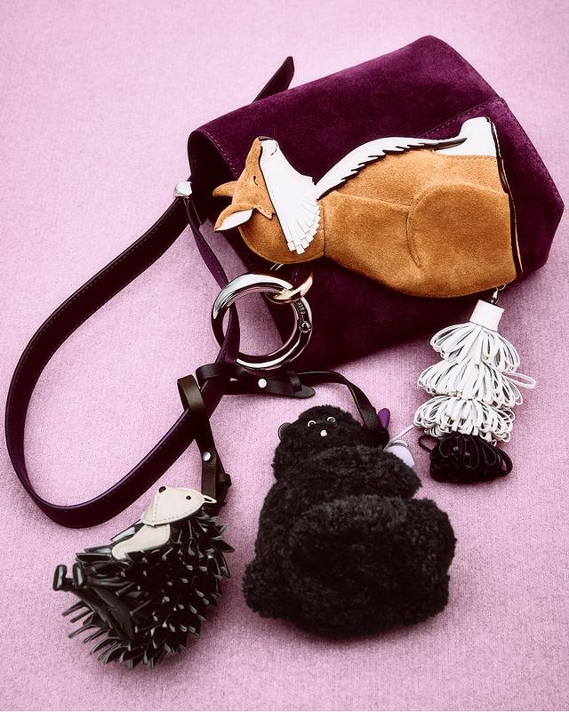 A purple handbag with a fox design, featuring playful, textured dog toy shapes attached. Set against a pink background, conveying a whimsical tone.