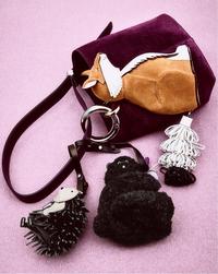 A purple handbag with a fox design, featuring playful, textured dog toy shapes attached. Set against a pink background, conveying a whimsical tone.
