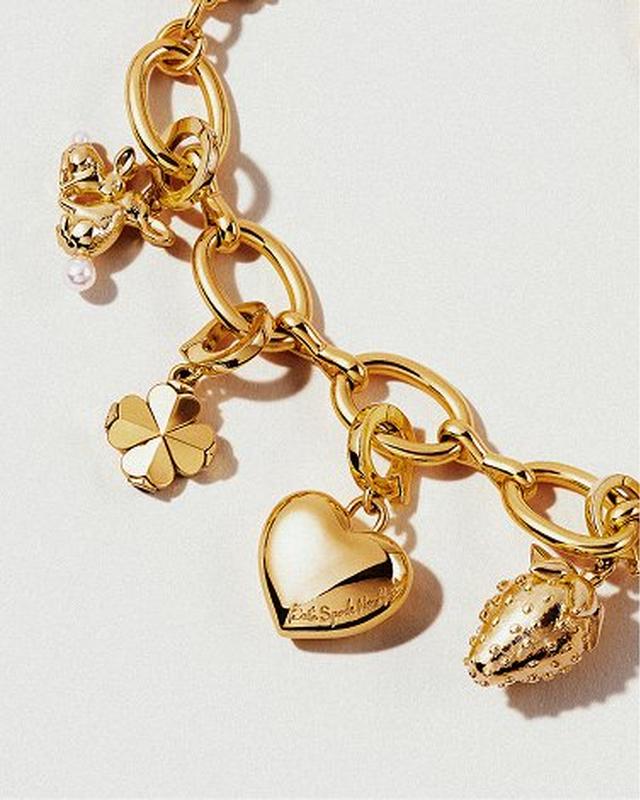 A gold charm bracelet with large links features charms of a rabbit, clover, heart, and strawberry, creating an elegant and playful tone.
