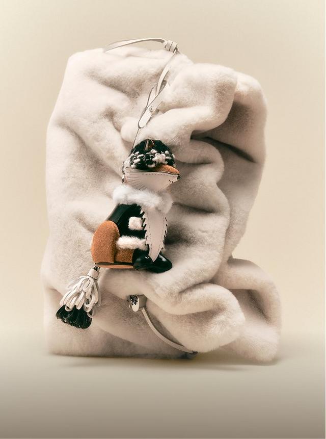 Cream faux fur drawstring bag with decorative charms and tassels attached to the closure.