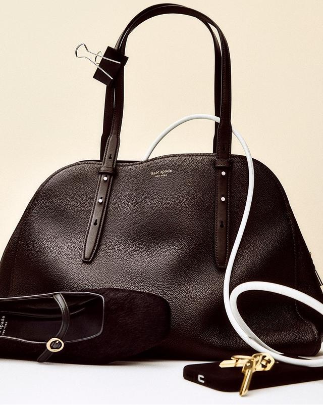 Elegant black leather handbag with gold accents, paired with a black shoe and white cable, set against a beige background. Sophisticated and classy.