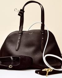 Elegant black leather handbag with gold accents, paired with a black shoe and white cable, set against a beige background. Sophisticated and classy.