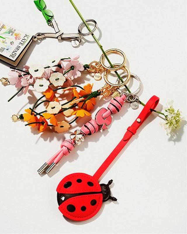 A colorful assortment of floral keychains and a red ladybug keychain on a white background. The keychains feature pink, white, and orange flowers.