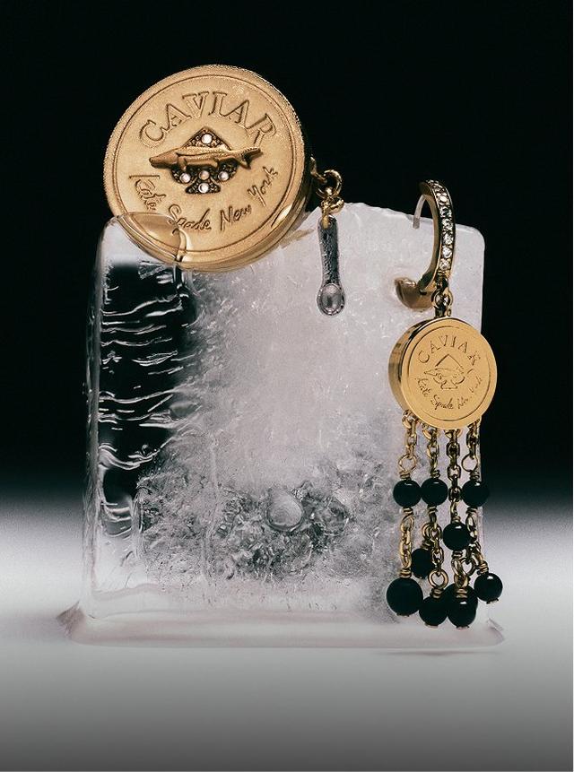 Caviar jewelry pieces with gold medallion lids and black bead details displayed on a frosted ice block.