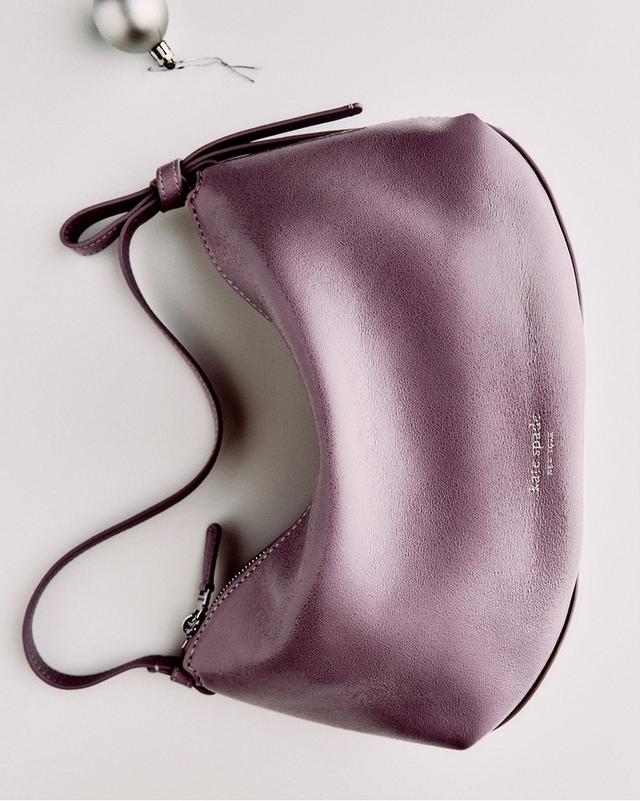 A purple leather handbag with a smooth finish, lying flat on a light surface. A silver ornament is placed nearby, adding a festive touch.