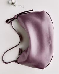 A purple leather handbag with a smooth finish, lying flat on a light surface. A silver ornament is placed nearby, adding a festive touch.