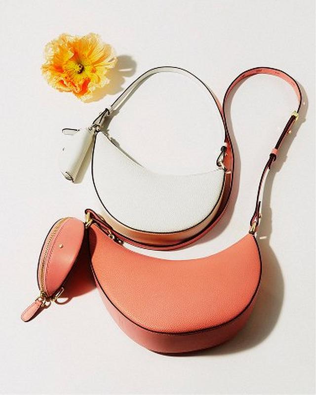 Two crescent-shaped handbags, one white and one coral, with matching coin purse on a white background. A vibrant yellow flower adds a cheerful accent.