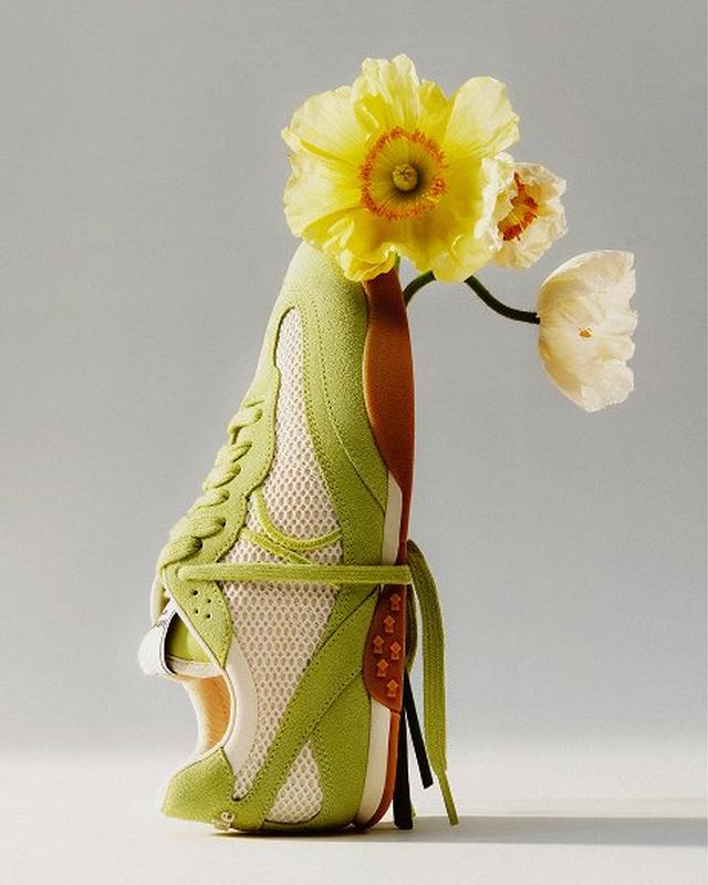A vibrant sneaker with green and white mesh stands on its heel against a neutral background. Yellow flowers emerge from the shoe, creating a fresh, whimsical vibe.