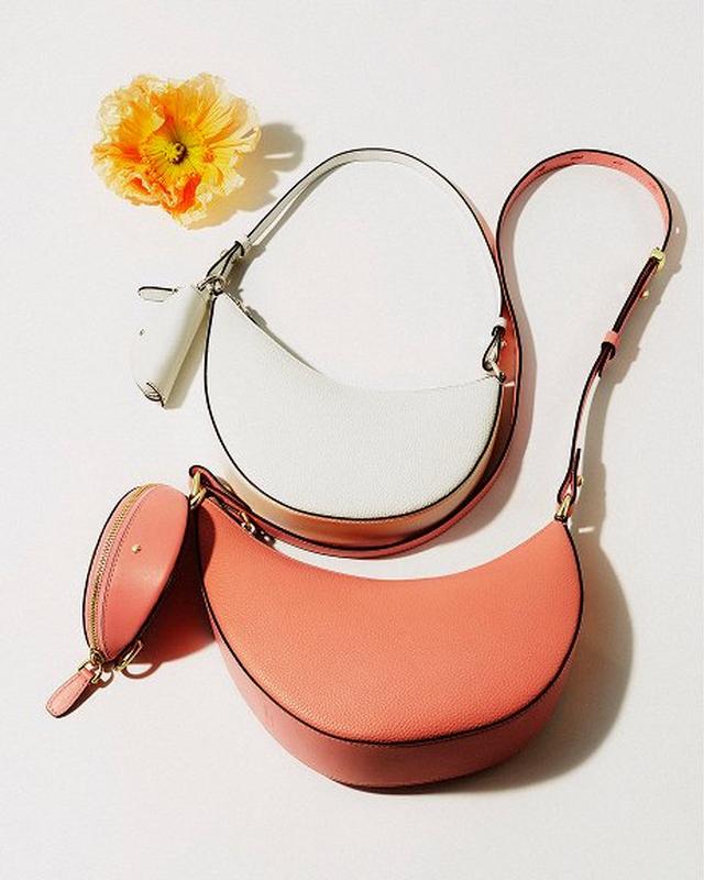 Two crescent-shaped handbags, one white and one coral, with matching coin purse on a white background. A vibrant yellow flower adds a cheerful accent.